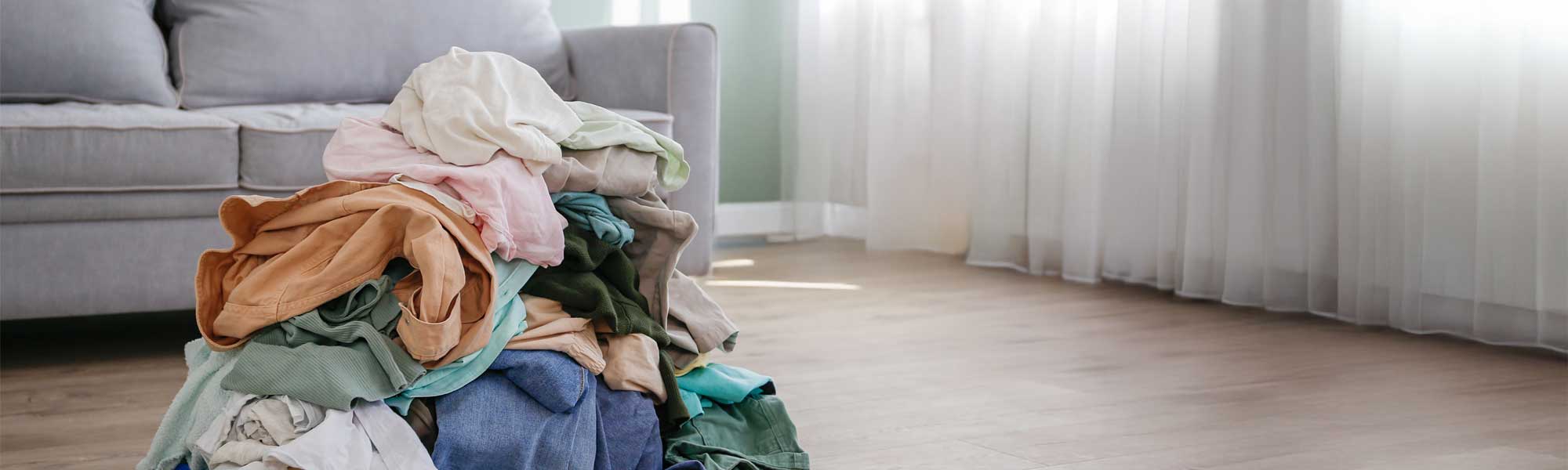 La foto mostra un cumulo di vestiti sul pavimento di una casa, pronti per diventare moda second-hand